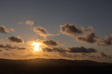 Dağ siluetlerinin günbatımı. Bulutlar, alacakaranlıkta güneşin altın ışıklarıyla aydınlanıyor. Fuerteventura, Kanarya Adaları, İspanya