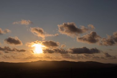 Dağ siluetlerinin günbatımı. Bulutlar, alacakaranlıkta güneşin altın ışıklarıyla aydınlanıyor. Fuerteventura, Kanarya Adaları, İspanya