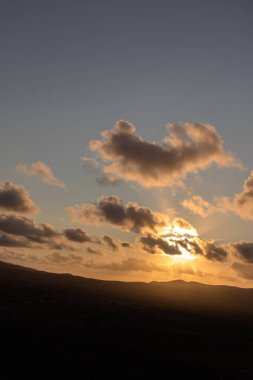 Dağ siluetlerinin günbatımı. Bulutlar, alacakaranlıkta güneşin altın ışıklarıyla aydınlanıyor. Fuerteventura, Kanarya Adaları, İspanya