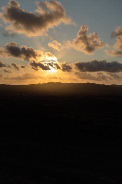 Dağ siluetlerinin günbatımı. Bulutlar, alacakaranlıkta güneşin altın ışıklarıyla aydınlanıyor. Fuerteventura, Kanarya Adaları, İspanya