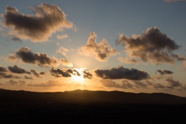 Dağ siluetlerinin günbatımı. Bulutlar, alacakaranlıkta güneşin altın ışıklarıyla aydınlanıyor. Fuerteventura, Kanarya Adaları, İspanya