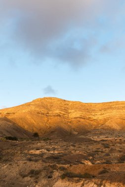 Dağ siluetlerinin günbatımı. Bulutlar, alacakaranlıkta güneşin altın ışıklarıyla aydınlanıyor. Fuerteventura, Kanarya Adaları, İspanya