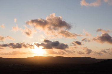 Dağ siluetlerinin günbatımı. Bulutlar, alacakaranlıkta güneşin altın ışıklarıyla aydınlanıyor. Fuerteventura, Kanarya Adaları, İspanya