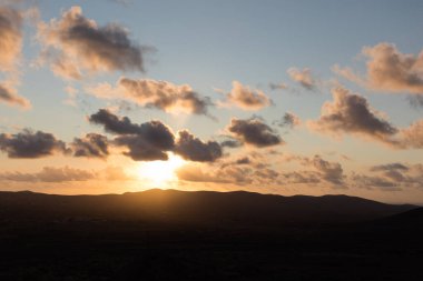 Dağ siluetlerinin günbatımı. Bulutlar, alacakaranlıkta güneşin altın ışıklarıyla aydınlanıyor. Fuerteventura, Kanarya Adaları, İspanya