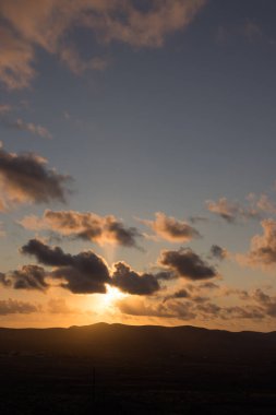 Dağ siluetlerinin günbatımı. Bulutlar, alacakaranlıkta güneşin altın ışıklarıyla aydınlanıyor. Fuerteventura, Kanarya Adaları, İspanya