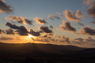 Dağ siluetlerinin günbatımı. Bulutlar, alacakaranlıkta güneşin altın ışıklarıyla aydınlanıyor. Fuerteventura, Kanarya Adaları, İspanya