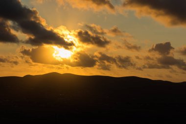 Dağ siluetlerinin günbatımı. Bulutlar, alacakaranlıkta güneşin altın ışıklarıyla aydınlanıyor. Fuerteventura, Kanarya Adaları, İspanya