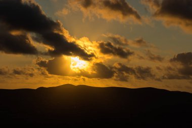 Dağ siluetlerinin günbatımı. Bulutlar, alacakaranlıkta güneşin altın ışıklarıyla aydınlanıyor. Fuerteventura, Kanarya Adaları, İspanya