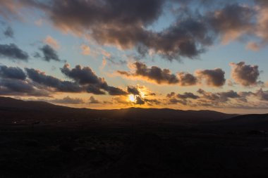 Dağ siluetlerinin günbatımı. Bulutlar, alacakaranlıkta güneşin altın ışıklarıyla aydınlanıyor. Fuerteventura, Kanarya Adaları, İspanya