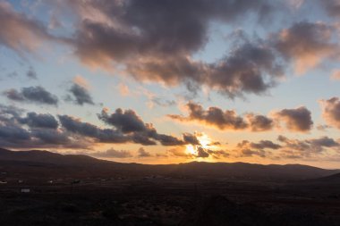 Dağ siluetlerinin günbatımı. Bulutlar, alacakaranlıkta güneşin altın ışıklarıyla aydınlanıyor. Fuerteventura, Kanarya Adaları, İspanya