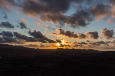 Dağ siluetlerinin günbatımı. Bulutlar, alacakaranlıkta güneşin altın ışıklarıyla aydınlanıyor. Fuerteventura, Kanarya Adaları, İspanya