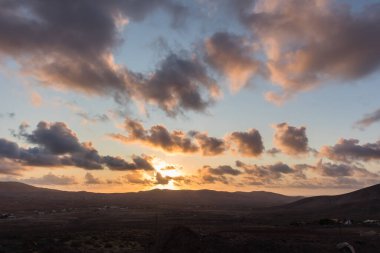 Dağ siluetlerinin günbatımı. Bulutlar, alacakaranlıkta güneşin altın ışıklarıyla aydınlanıyor. Fuerteventura, Kanarya Adaları, İspanya