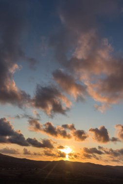 Dağ siluetlerinin günbatımı. Bulutlar, alacakaranlıkta güneşin altın ışıklarıyla aydınlanıyor. Fuerteventura, Kanarya Adaları, İspanya