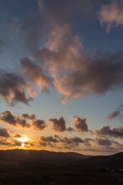 Dağ siluetlerinin günbatımı. Bulutlar, alacakaranlıkta güneşin altın ışıklarıyla aydınlanıyor. Fuerteventura, Kanarya Adaları, İspanya
