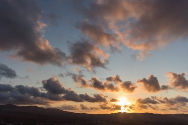 Dağ siluetlerinin günbatımı. Bulutlar, alacakaranlıkta güneşin altın ışıklarıyla aydınlanıyor. Fuerteventura, Kanarya Adaları, İspanya