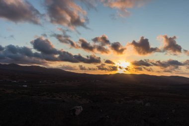 Dağ siluetlerinin günbatımı. Bulutlar, alacakaranlıkta güneşin altın ışıklarıyla aydınlanıyor. Fuerteventura, Kanarya Adaları, İspanya