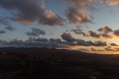 Dağ siluetlerinin günbatımı. Bulutlar, alacakaranlıkta güneşin altın ışıklarıyla aydınlanıyor. Fuerteventura, Kanarya Adaları, İspanya