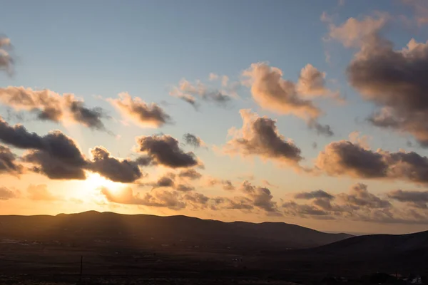 Dağ siluetlerinin günbatımı. Bulutlar, alacakaranlıkta güneşin altın ışıklarıyla aydınlanıyor. Fuerteventura, Kanarya Adaları, İspanya