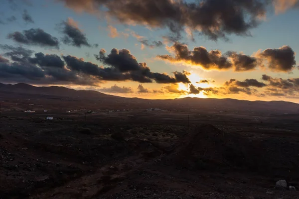 Dağ siluetlerinin günbatımı. Bulutlar, alacakaranlıkta güneşin altın ışıklarıyla aydınlanıyor. Fuerteventura, Kanarya Adaları, İspanya