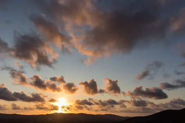 Dağ siluetlerinin günbatımı. Bulutlar, alacakaranlıkta güneşin altın ışıklarıyla aydınlanıyor. Fuerteventura, Kanarya Adaları, İspanya