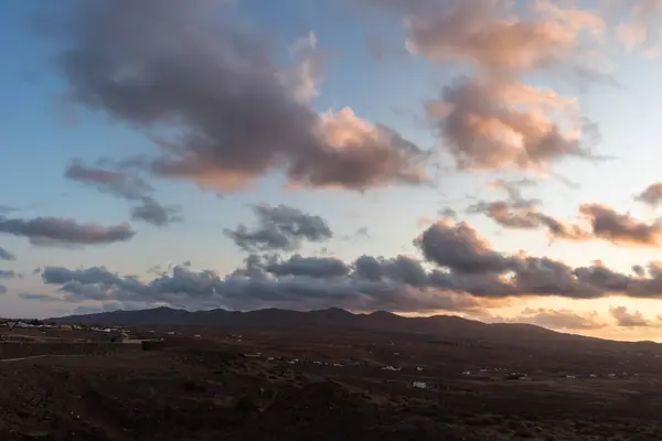 Dağ siluetlerinin günbatımı. Bulutlar, alacakaranlıkta güneşin altın ışıklarıyla aydınlanıyor. Fuerteventura, Kanarya Adaları, İspanya