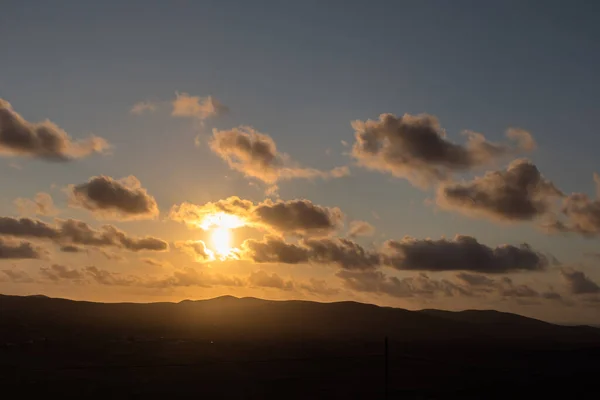 Dağ siluetlerinin günbatımı. Bulutlar, alacakaranlıkta güneşin altın ışıklarıyla aydınlanıyor. Fuerteventura, Kanarya Adaları, İspanya