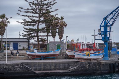 Rıhtımdaki mavi antika vinç. Geleneksel ahşap tekneler, beyaz mavi ve kırmızı, iskelede denizin dışından. Puerto de la Cruz, Tenerife, Kanarya Adaları, İspanya.
