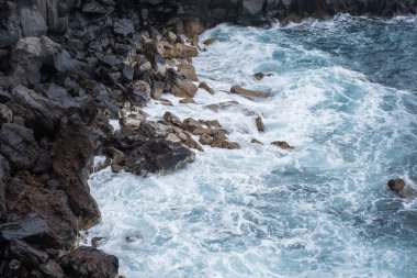 Uçurumun taşları. Dalgalar uçurumun volkanik kayalarına çarpıyor. Dalgalı okyanus. Siyah kayalar. Puerto de la Cruz, Tenerife, Kanarya Adaları, İspanya.