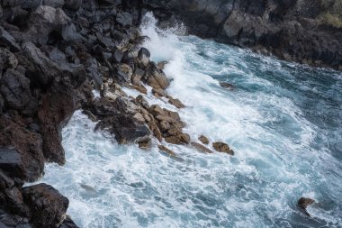 Uçurumun taşları. Dalgalar uçurumun volkanik kayalarına çarpıyor. Dalgalı okyanus. Siyah kayalar. Puerto de la Cruz, Tenerife, Kanarya Adaları, İspanya.