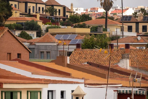 Solar panels on red tile roofs of single-family houses in a village. Palm trees and trees in the background. Tenerife, Canary Islands, Spain