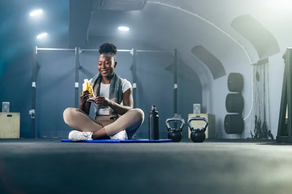 Подходит Афроамериканка Спортивной Одежде Ест Банан Спортзале После Тренировки Сидит Стоковое Изображение