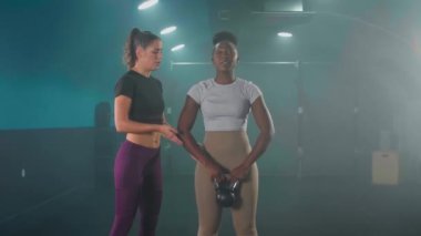 Fitness gym instructor showing correct pose with kettlebell to young African American woman in sportswear
