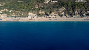 Güneş gözlüklü ve yumuşak turkuaz okyanus dalgalı güzel kumlu sahil manzarası. Yaz mevsiminde Lefkada adasındaki Kathisma plajında tropik deniz..