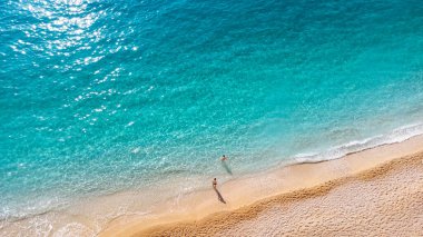 Yumuşak turkuaz okyanus dalgalarıyla güzel kumlu sahilde duran çiftin hava manzarası. Yaz mevsiminde Lefkada adasındaki Porto Katsiki plajında tropik deniz.