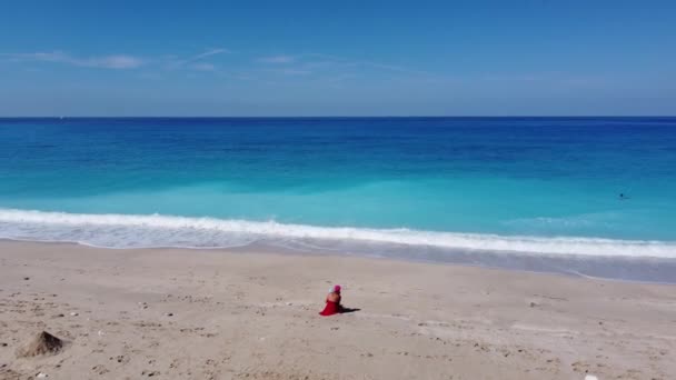 空中俯瞰着身穿红色衣服的女人 她们抱着孩子坐在沙滩上 享受着柔和的绿松石海浪 Lefkada岛上Megali Petra海滩夏季热带海域 — 图库视频影像