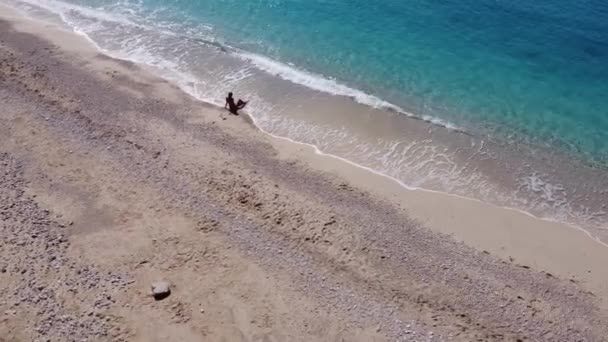 在空中俯瞰着身穿泳衣的美丽快乐女人 她坐在浅海的沙滩上 享受着海滩和柔和的绿松石海浪 Lefkada岛上Egremni海滩夏季热带海域 — 图库视频影像