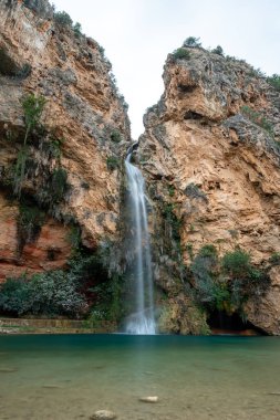 İspanya, Valencia, Buol 'da bitki örtüsü ve kayalarla çevrili bir şelalenin dikey manzarası.