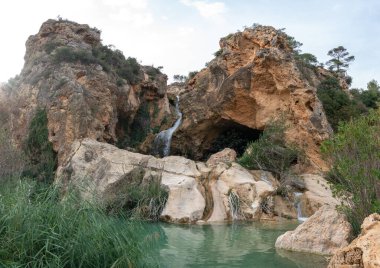 İspanya, Valencia, Buol 'da bitki örtüsü ve kayalarla çevrili Las Paloma mağarasında bir şelale manzarasının güzel manzarası.