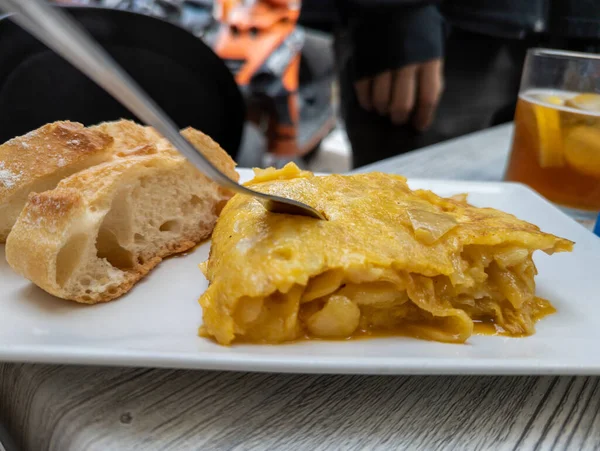 Hafif dondurulmuş yumurtayla lezzetli patates omleti, yanında iki parça ekmek ve omlete saplanmış bir çatal, tipik İspanyol tapası.
