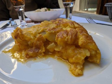 Beautiful profile photo of a potato omelette with a very tasty golden onion on the outside where you can see perfectly the potato wedges and the liquid egg in it with a background of beer and salad