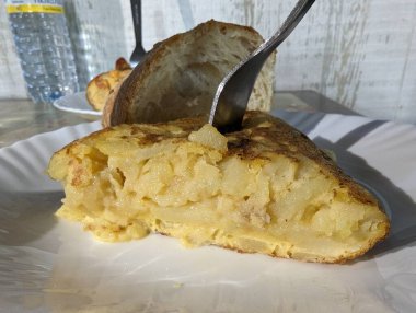 Beautiful profile shot of a potato omelette with onion and cheese on the bottom very tasty with a piece of bread and the fork stuck in the omelette on top