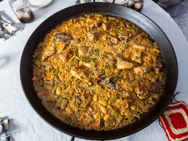 Tipik bir Valensiyalı paella 'nın güzel genel manzarası. Orijinal malzemeli tavuk, tavşan, yeşil ve beyaz fasulye. Buzlu, tabaklı, çatal bıçaklı ve peçeteli bir masada. Nefis ev yapımı paella, orijinal Valensiyalı paella..