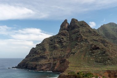 Yeşil alanlarla dolu kayalık bir dağ ile güzel kıyı manzarası, okyanus sularında güzel renkler ve gökyüzünde bulutlar, Tenerife, Kanarya Adaları, İspanya, Avrupa