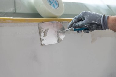Ressam, inşaat sahasında bir spatulayla iç duvarı yeniliyor.