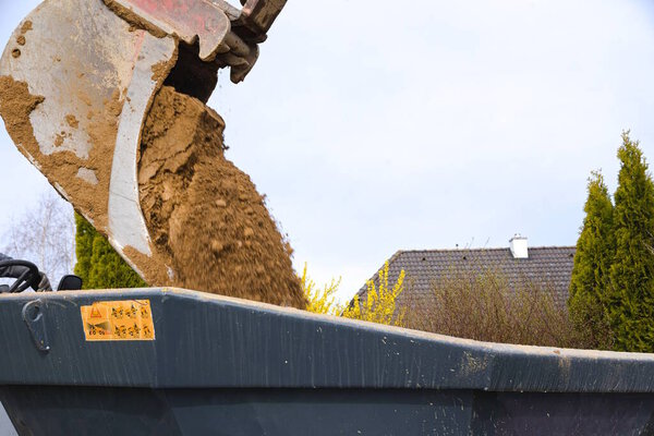 Bucket of backhoe at construction site dumps earth into dump truck - close-up