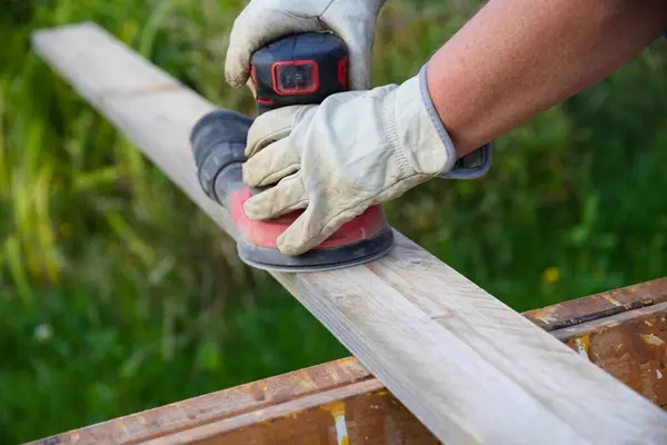 stock image Skilled worker sands wooden board by hand with sander - eccentric sander