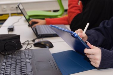 Student writes on tablet and works on laptop - close-up clipart