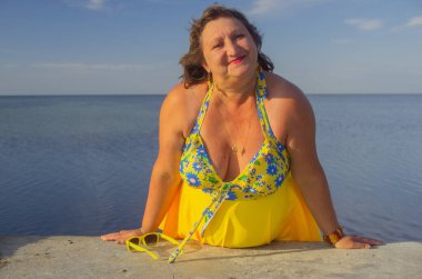 Denize karşı sarı mayo giymiş orta yaşlı bir kadının portresi.