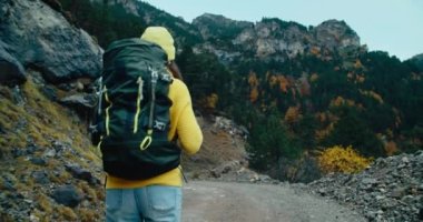 Sonbahar haftasonu seyahati yapan bir kadın sırt çantasıyla çakıllı dağ yolunda yürüyor. Tatil gezisinde sarı kazaklı bir kadın yolcu. El kamerasıyla, seyahat macerasının gösterişsiz görüntüsü seyahat tutkusu 