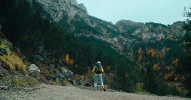Sırt çantasıyla dağ yolunda sonbahar tatili yapan tek kişilik gezginin el kamerası görüntüsü. Gösterişsiz sinemadaki sarı kazaklı kadın destansı manzarada yürüyüş yapıyor. Seyahat macerası seyahat tutkusu